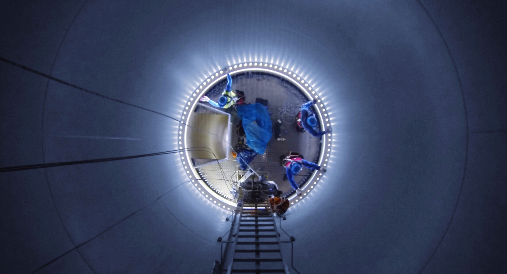 An image taken inside a windmill from above, with several workers on groundlevel working on maintenance. 