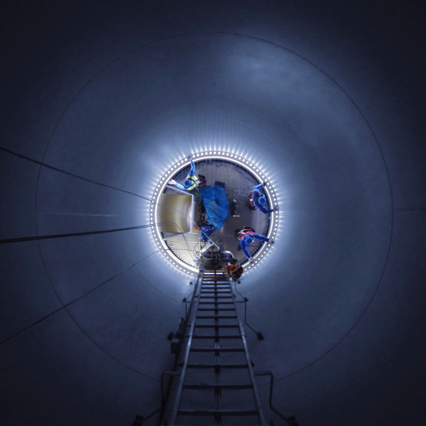 An image taken inside a windmill from above, with several workers on groundlevel working on maintenance. 