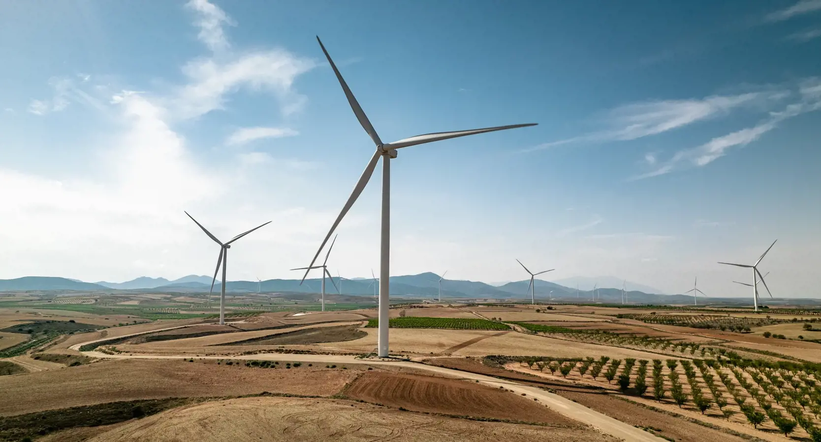 An image of an onshore windmill farm. The windmils are situated by a trail in an area of agriculture in Aragon, Spain.