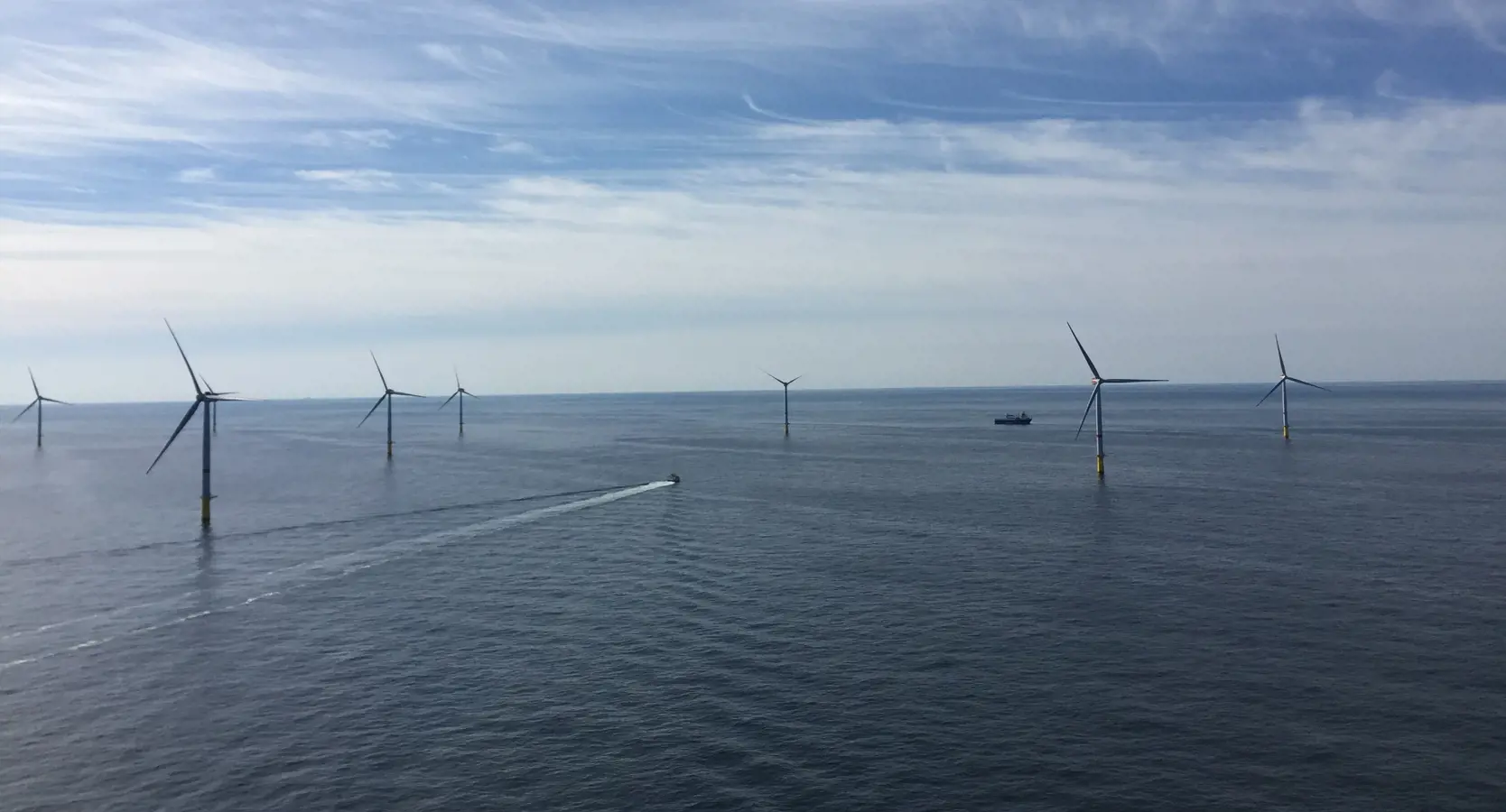 An image of a windmill farm situated in the ocean. Two ships are sailing between the windmills. The offshore windmill park is called: the Changfang and Xidao Offshore Wind Project.